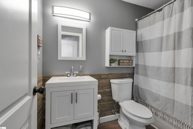 bathroom featuring a textured ceiling, toilet, a shower with curtain, wooden walls, and vanity