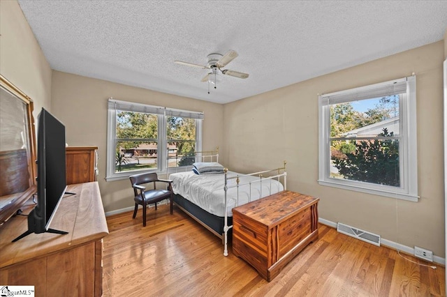 bedroom with ceiling fan, a textured ceiling, multiple windows, and light wood-type flooring