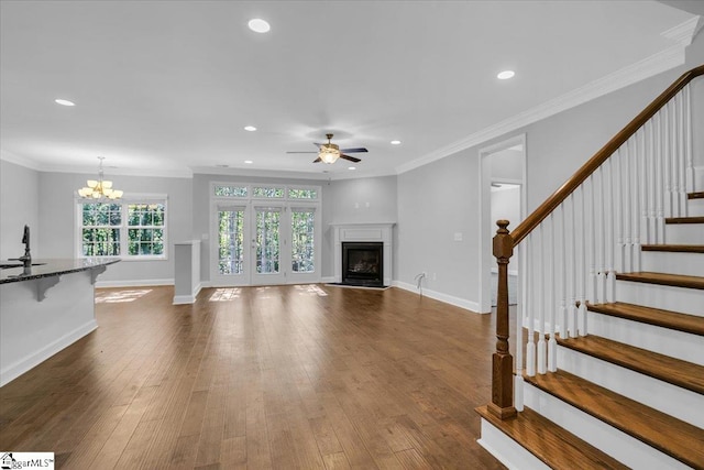 unfurnished living room with crown molding, ceiling fan with notable chandelier, and dark hardwood / wood-style flooring