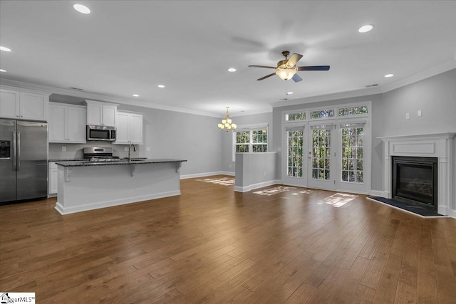 unfurnished living room with ornamental molding, dark hardwood / wood-style flooring, and ceiling fan with notable chandelier