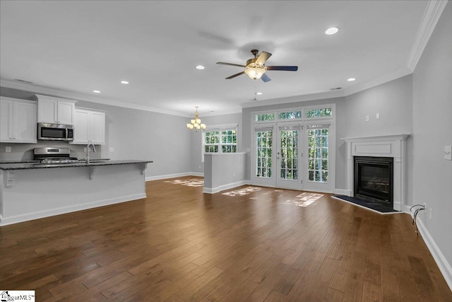 unfurnished living room with sink, dark wood-type flooring, crown molding, and ceiling fan with notable chandelier