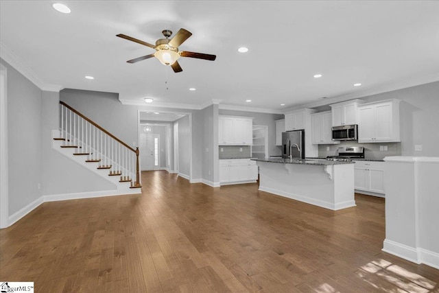 kitchen featuring a kitchen island with sink, wood-type flooring, stainless steel appliances, dark stone countertops, and white cabinets