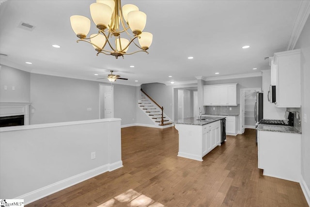 kitchen with an island with sink, white cabinetry, pendant lighting, dark stone countertops, and hardwood / wood-style flooring