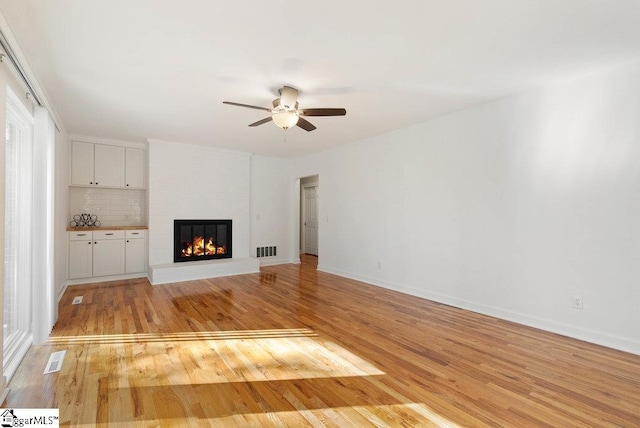 unfurnished living room with light hardwood / wood-style flooring, ceiling fan, a fireplace, and plenty of natural light