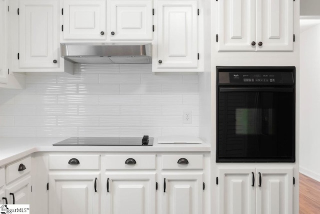 kitchen with tasteful backsplash, black appliances, white cabinetry, wall chimney exhaust hood, and light hardwood / wood-style flooring