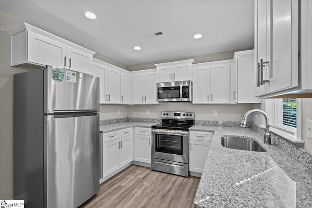 kitchen with white cabinets, light stone counters, light hardwood / wood-style flooring, sink, and stainless steel appliances