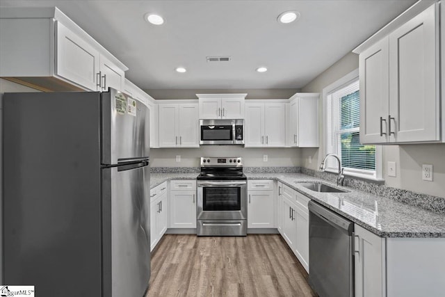 kitchen with light stone countertops, sink, white cabinets, and stainless steel appliances