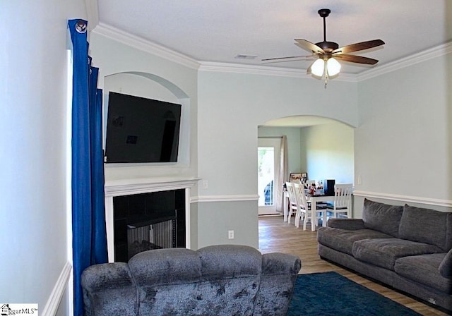 living room with ceiling fan, crown molding, a tiled fireplace, and hardwood / wood-style floors