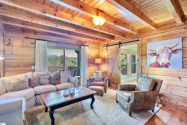 living room featuring wood walls, wood-type flooring, beamed ceiling, and a barn door