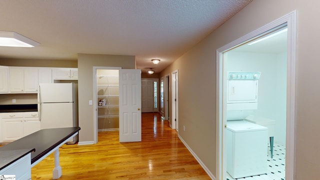 kitchen with white cabinets, a textured ceiling, light hardwood / wood-style floors, stacked washer and clothes dryer, and white refrigerator