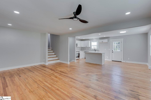 unfurnished living room with an AC wall unit, sink, light wood-type flooring, and ceiling fan