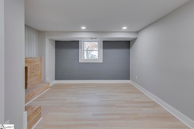 basement with brick wall and light wood-type flooring