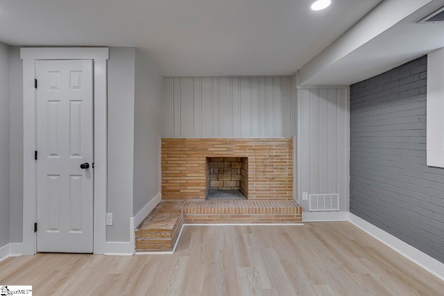 unfurnished living room featuring a fireplace, wood walls, brick wall, and light wood-type flooring