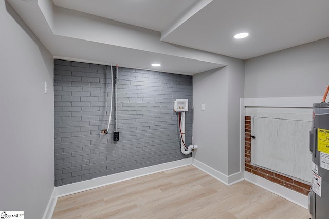 washroom with brick wall, water heater, and light wood-type flooring