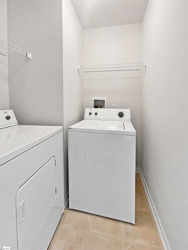 laundry area with a textured ceiling, light tile patterned flooring, and washing machine and clothes dryer