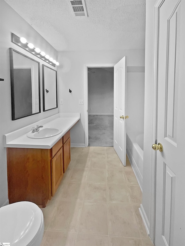 bathroom featuring a tub, a textured ceiling, toilet, tile patterned floors, and vanity