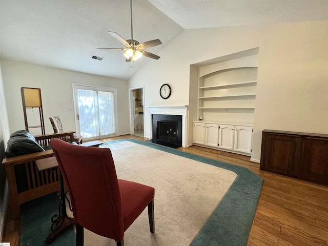 living room with a textured ceiling, hardwood / wood-style flooring, ceiling fan, and vaulted ceiling