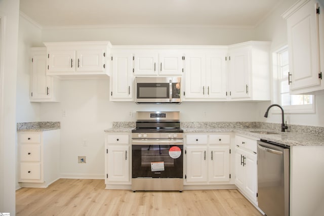 kitchen featuring appliances with stainless steel finishes, white cabinetry, light hardwood / wood-style floors, crown molding, and sink