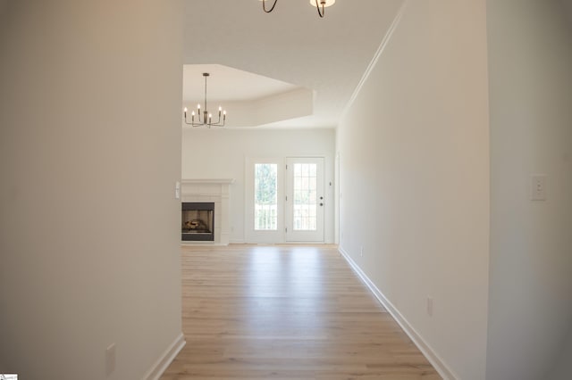 corridor featuring light hardwood / wood-style floors, crown molding, a tray ceiling, and a chandelier