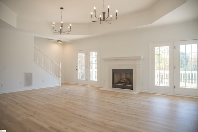 unfurnished living room with light hardwood / wood-style flooring, ornamental molding, a tiled fireplace, and a tray ceiling