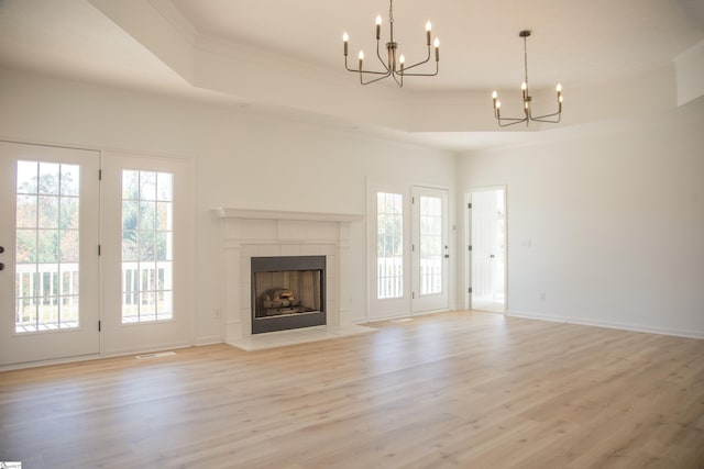 unfurnished living room with light hardwood / wood-style flooring, a tray ceiling, a tile fireplace, crown molding, and a chandelier