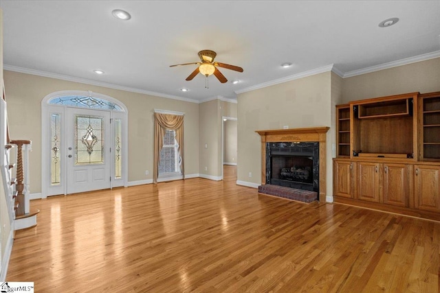 unfurnished living room with ceiling fan, ornamental molding, a brick fireplace, and light wood-type flooring