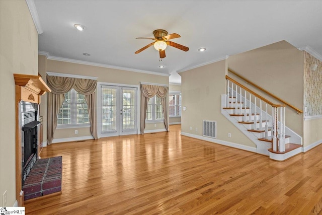 unfurnished living room with ceiling fan, light hardwood / wood-style flooring, crown molding, a fireplace, and french doors