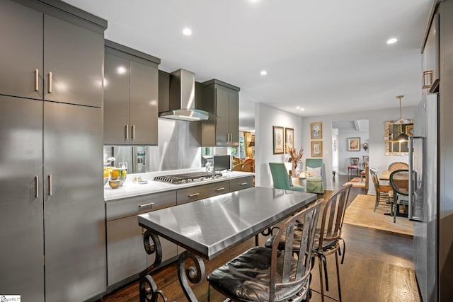 kitchen featuring a kitchen bar, stainless steel appliances, wall chimney exhaust hood, gray cabinets, and dark hardwood / wood-style floors