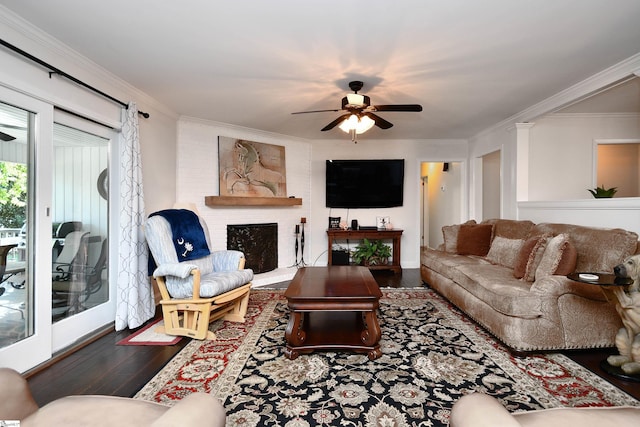 living room featuring ceiling fan, crown molding, a brick fireplace, and dark hardwood / wood-style floors