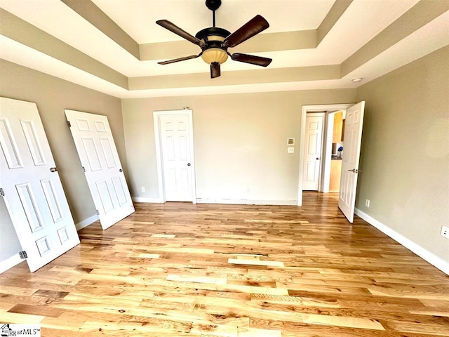 unfurnished bedroom with light hardwood / wood-style floors, a tray ceiling, and ceiling fan