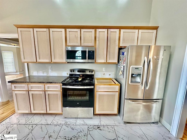 kitchen featuring appliances with stainless steel finishes, dark stone counters, light brown cabinetry, and light wood-type flooring