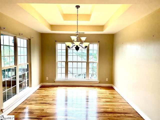 unfurnished dining area with a notable chandelier, a tray ceiling, and light wood-type flooring