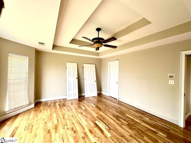 unfurnished bedroom featuring light hardwood / wood-style flooring, a tray ceiling, and ceiling fan