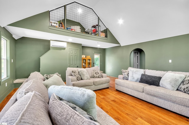 living room with an AC wall unit, a healthy amount of sunlight, wood-type flooring, and high vaulted ceiling