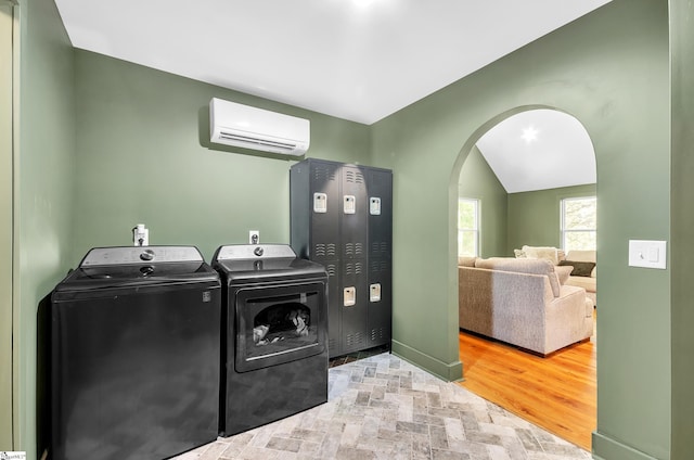 washroom featuring a wall unit AC, independent washer and dryer, and light hardwood / wood-style flooring