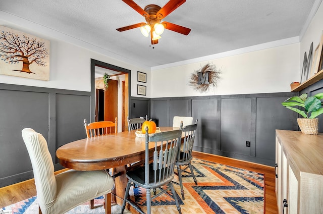 dining area featuring ceiling fan, a textured ceiling, ornamental molding, and light wood-type flooring