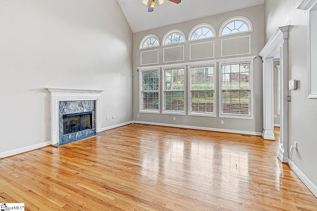 unfurnished living room featuring ceiling fan, a high end fireplace, light hardwood / wood-style flooring, and high vaulted ceiling