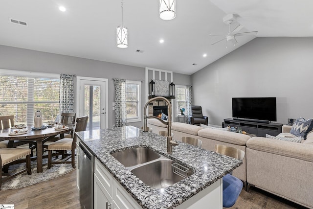 kitchen featuring lofted ceiling, hanging light fixtures, dark stone countertops, stainless steel dishwasher, and white cabinetry