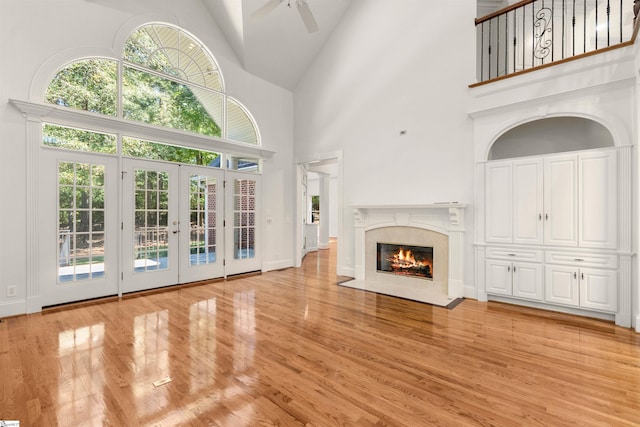 unfurnished living room featuring french doors, light hardwood / wood-style floors, a high ceiling, and ceiling fan