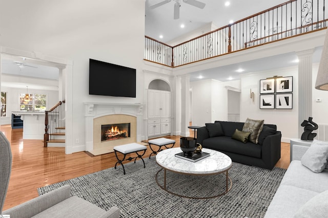 living room featuring ceiling fan, wood-type flooring, ornate columns, a high ceiling, and crown molding