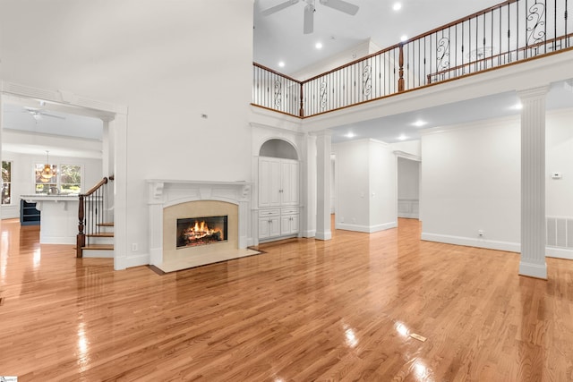 unfurnished living room featuring ornate columns, light hardwood / wood-style flooring, and a high ceiling