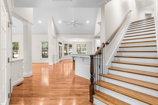 foyer with ornate columns, high vaulted ceiling, light wood-type flooring, and ceiling fan with notable chandelier