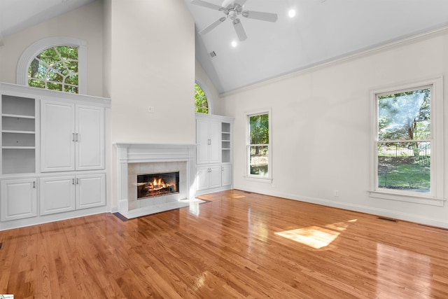 unfurnished living room with light hardwood / wood-style floors, high vaulted ceiling, a tile fireplace, and ceiling fan