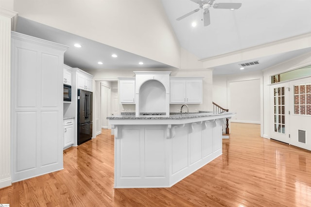 kitchen featuring a kitchen breakfast bar, black appliances, light wood-type flooring, white cabinetry, and high vaulted ceiling