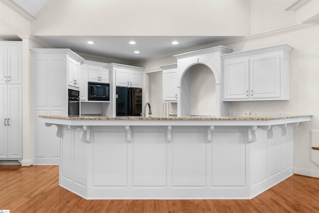 kitchen featuring black appliances, ornamental molding, light wood-type flooring, and white cabinets