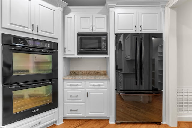 kitchen with light stone countertops, black appliances, light wood-type flooring, and white cabinets