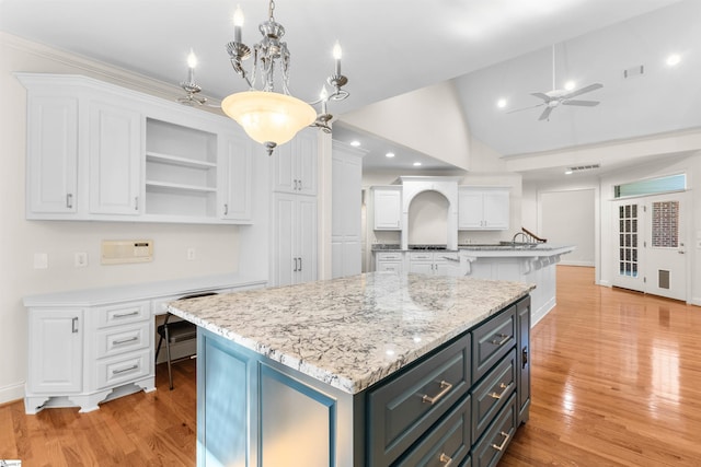 kitchen with built in desk, a center island, light hardwood / wood-style floors, lofted ceiling, and white cabinets