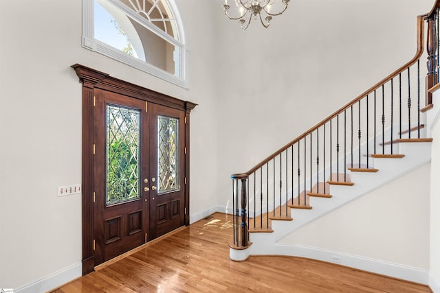 foyer entrance with french doors, a towering ceiling, wood-type flooring, and a chandelier