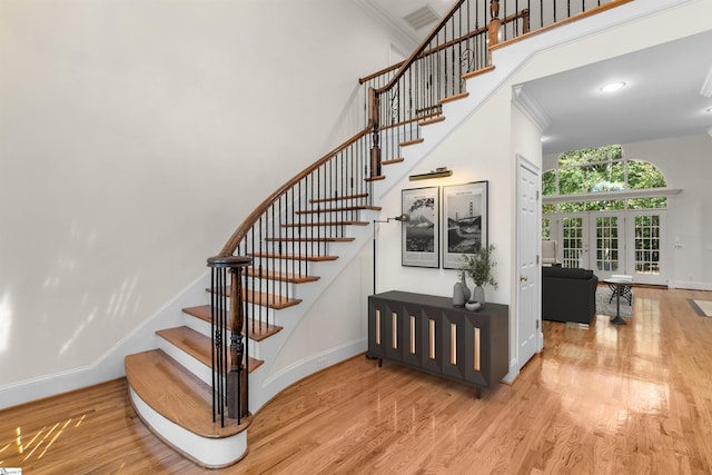 stairs featuring a towering ceiling, crown molding, hardwood / wood-style floors, and french doors