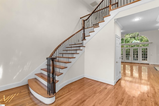 stairs with ornamental molding, hardwood / wood-style floors, french doors, and a high ceiling